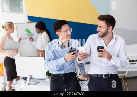 Männliche Helpdesk-Mitarbeiter, die während der Kaffeepause im modernen Callcenter auf dem Smartphone im Internet surfen, Speicherplatz kopieren Stockfoto