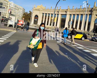 Junge Frau in Maske überquert die Straße auf einem Zebrastreifen. Sie trägt eine hängende Tasche und eine leere Einkaufstasche. Stockfoto