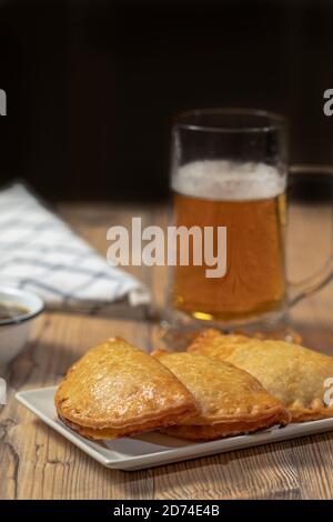 Argentinier Fleisch Empanadas mit einem Glas Bier über ein Holztisch Stockfoto