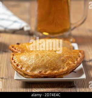 Argentinier Fleisch Empanadas mit einem Glas Bier über ein Holztisch Stockfoto