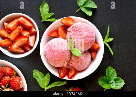 Erdbeereis in Schale auf dunklem Steinhintergrund. Kalter Sommerdessert. Draufsicht, flach liegend Stockfoto