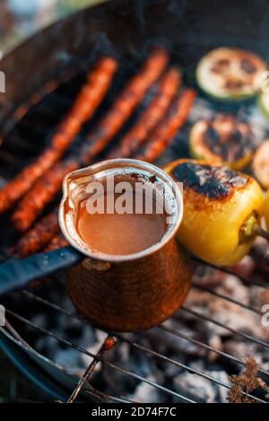 Eine türkische Kaffeekanne mit Würstchen und etwas Gemüse auf einem Grill. Stockfoto