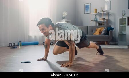 Starker Athletic Fit Mann in T-Shirt und Shorts macht Bergsteiger Übungen, während mit einer Stoppuhr auf seinem Handy. Er bildet zu Hause in seinem aus Stockfoto