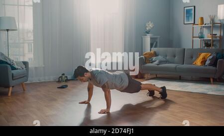 Muscular Athletic Fit man in T-Shirt und Shorts macht Push-up-Übungen zu Hause in seinem geräumigen und sonnigen Wohnzimmer mit modernem Interieur. Stockfoto