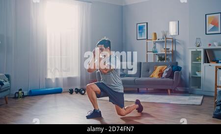 Starke Athletic Fit Mann in T-Shirt und Shorts tut Vorwärts Ausfallschritt Übungen zu Hause in seiner geräumigen und hellen Wohnung mit minimalistischem Interieur Stockfoto