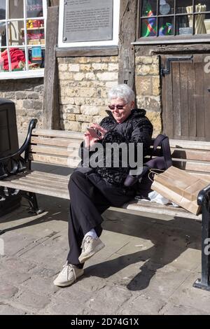 Lächelnde ältere Frau, die im Freien nach Mobiltelefonen schaut, Großbritannien Stockfoto
