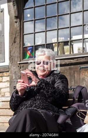 Lächelnde ältere Frau, die im Freien nach Mobiltelefonen schaut, Großbritannien Stockfoto