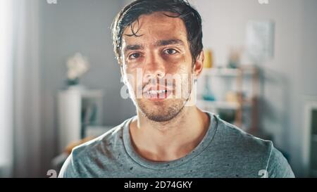 Schwitzen muskulös Athletic Fit Mann in Grau Outfit posiert nach einem Workout zu Hause in seinem geräumigen und sonnigen Wohnzimmer mit minimalistischem Interieur. Stockfoto