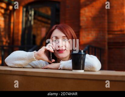 Lächelnde Frau lehnte sich auf dem Bartisch und sprach auf dem Handy. Frau, die mit einem Freund am Telefon chattet. Stockfoto