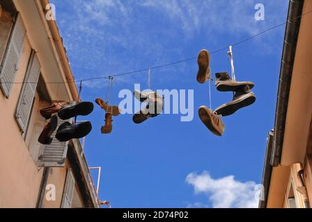 Provence auf einem Schuhschnur: Sportschuhe und andere Schuhe schwingen in der Brise über einer schmalen Seitenstraße direkt am zentralen Place de l’université in Aix-en-Provence, Bouches-du-Rhône, Provence-Alpes-Côte d’Azur, Frankreich. Stockfoto