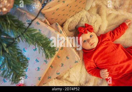 Erste weihnachten für Mädchen unter dem Baum - Neugeborenes in rotem Kleid, das um die Geschenke herum liegt- Familie Konzept Stockfoto