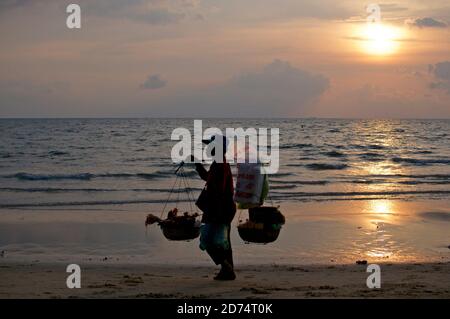 Otres Beach, Sihanoukville, Kambodscha - 30. Dezember 2018 : Silhouette einer traditionellen weiblichen Lebensmittelverkäuferin bei Sonnenuntergang am Strand von Otres Beach i Stockfoto