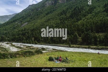 Traditionelle Familie teilen Mittagessen und Ernte Erbsen umgeben von Himalaya, Pinienwald und Fluss in Chitkul, Himachal Pradesh, Indien. Stockfoto