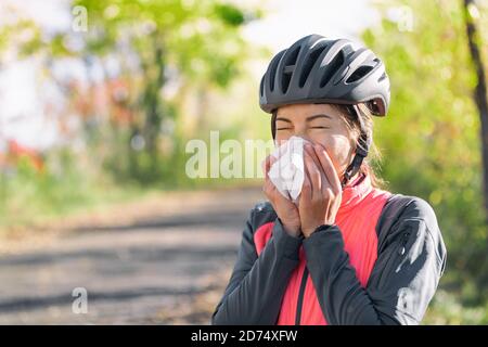 Husten im Gewebe, das Nase und Mund bedeckt, wenn es draußen hustet, als COVID-19-Hygienerichtlinie zur Verhinderung der Verbreitung des Coronavirus. Radfahren Radfahrer Mädchen Stockfoto