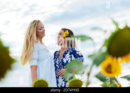 Paar attraktive Frauen eine Blondine und die andere Brünette Posiert in ihren Designer-Kleidern in einem Feld von Sonnenblumen Stockfoto