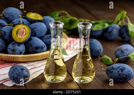 Pflaumenbrand oder Schnaps in kleinen Glasflaschen mit frischen und leckeren Pflaumen auf einem Holztisch. Selektiver Fokus. Stockfoto