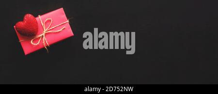 Rosa Geschenkbox und rotes Herz auf schwarzem Hintergrund. Banner. Geschenk zum Valentinstag, Geburtstag oder Muttertag. Draufsicht, Kopierbereich Stockfoto