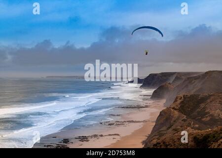 Vila do Bispo, Portugal - 12. Februar 2020: Ein Gleitschirm, der über die malerischen Klippen am Strand von Cordoama (Praia da Cordoama) in der Nähe des Dorfes fliegt Stockfoto