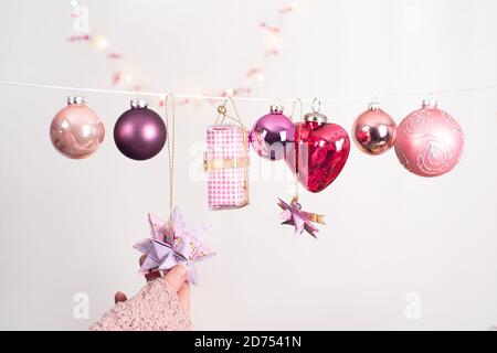 Weihnachtsbild mit verschiedenen Kugeln in den Farben der Beeren. Kleines Geschenk und Baumanhänger, der an einer Schnur hängt. Die Hand einer Frau berührt einen Fröbelster Stockfoto