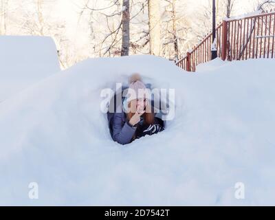 Lächelndes Mädchen zeigt Siegeszeichen mit Fingern aus schauen Schneetunnel Stockfoto