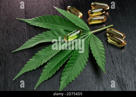 Kapseln oder Pillen mit CBD-Cannabis oder Hanföl auf dem Blatt von Marihuana auf dem schwarzen Holzhintergrund. Konzept der alternativen Medizin. Stockfoto