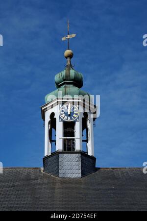 Alter Kirchturm mit goldener Uhr und grünem Dach. Wetterfahne auf dem Dach. Es ist zwölf Uhr. Blauer Himmel. Stockfoto