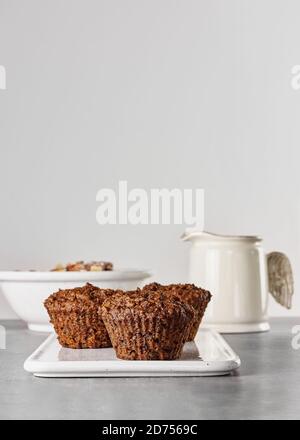Gesundes Frühstück. Karotten vegane Muffins, Müsli oder Müsli auf weißer Schale und Glas Milch auf grauem Steintisch. Kinfolk-Stil. Stockfoto