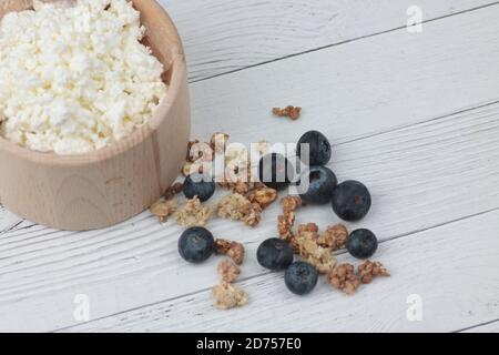 Holzschale mit Bauernkäse, Heidelbeere und Müsli auf weißem Holzhintergrund flach legen. Gesunde Ernährung Konzept. Das Bild enthält den Kopierbereich Stockfoto