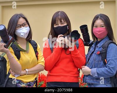 Drei vietnamesische Straßenfotografinnen tragen Schutzmasken und posieren mit ihrer Fotoausrüstung während der Corona-Pandemie. Stockfoto