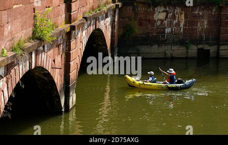 Eltern und Kind mit Hüten auf in aufblasbaren Kajak gehen Unter der niedrigen Brücke Stockfoto