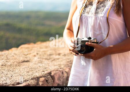 Die junge Frau hält eine alte Kamera, die an ihrem Hals neben einer Steinwand hängt. Fotokonzept Stockfoto