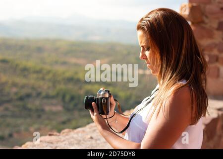 Eine junge Frau hält eine alte Kamera und lernt, wie man sie vor einer Landschaft benutzt. Fotokonzept Stockfoto