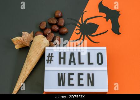 Text Halloween auf schwarz-orangenen Hintergrund, Waffel Eiscreme Kegel mit Kastanien und dekorative Fledermaus und Spinne. Grußkarte oder Party Einladung desig Stockfoto