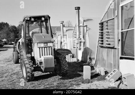 Ein John Deere Landtraktor, der einen Pul-Blast-Feldspritzenwagen zieht, wird vor mehreren Gewächshäusern auf einer Farm in New Hampshire geparkt. Herbstlaub ist in Th Stockfoto