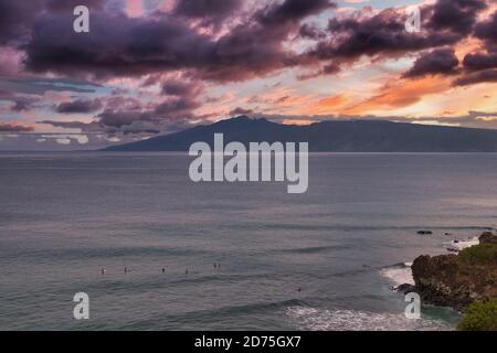 Surfer sitzen auf ihren Brettern in Honolua Bay auf Maui bei Sonnenuntergang. Stockfoto