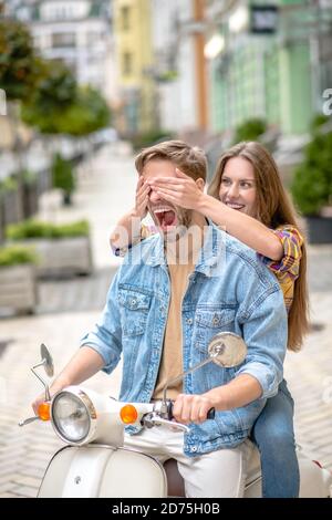 Frau, die die Augen von mans schließt, während sie einen Roller fährt Stockfoto