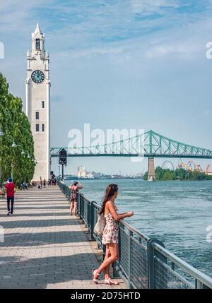 Montreal Old Port Harbour Frau, die auf der Stadtstraße mit Blick auf den St. Lawrence River mit Jacques Cartier Brücke und Tour de l'Horloge auf geht Stockfoto