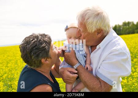 Glückliche Großeltern mit kleinen Baby Enkelin genießen Moment in schön Gelbes Feld Stockfoto