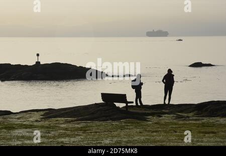 Zwei Frauen stehen silhouetted, während sie einen morgendlichen Chat in einem Park in der Nähe von Victoria auf Vancouver Island, British Columbia, Kanada Stockfoto