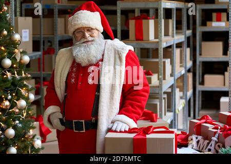Happy Santa Claus trägt Kostüm posiert in der Werkstatt mit Geschenken, Porträt. Stockfoto