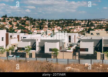 Viele Wohnvillen vor dem Hintergrund von Häusern in Israel, mit Garagen und Autos und einem Zaun, vor dem Hintergrund eines blauen Himmels mit Wolken. N Stockfoto