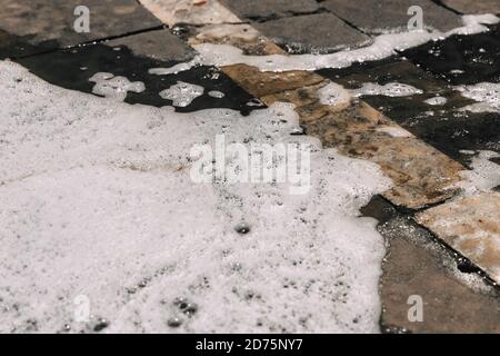 Schaum strömt auf dem Asphalt von Autowaschanlage, nasse Betonstruktur. Hintergrund im Hintergrund. Komplizierte natürliche Muster aus Schaum und Seifenblasen. Schwarzes tarma Stockfoto