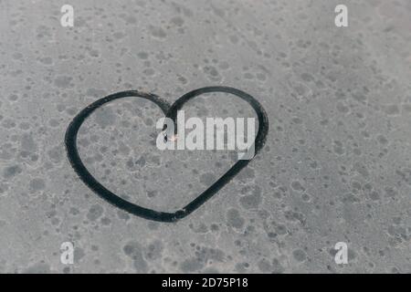 Herzsymbol auf schmutzigem Autofenster. Herz gezeichnet mit einem Finger auf das blendende Seitenfenster eines Autos. Fingerbemaltes Herz. Valentinstag romantische Zeichnung. Stockfoto