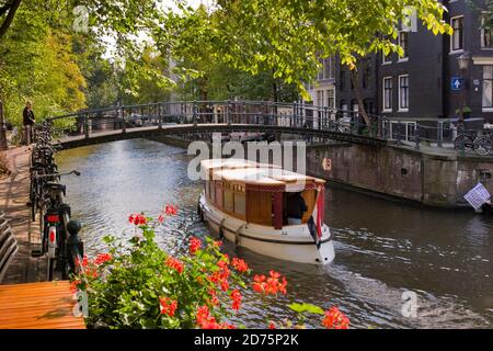 Eine typische Szene auf Amsterdams Grachten. Ein schön gepflegter Lastkahn, der jetzt für kleine Partys genutzt wird, macht seinen Weg unter einem der gewölbten Fußgänger fo Stockfoto