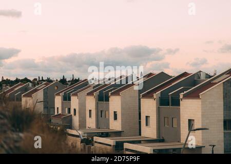 Viele Wohnvillen vor dem Hintergrund von Häusern in Israel, mit Garagen und Autos und einem Zaun, vor dem Hintergrund eines blauen Himmels mit Wolken. N Stockfoto