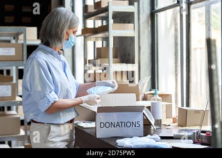 Ältere weibliche Freiwillige tragen Maske Verpackung medizinische Spenden Box. Stockfoto