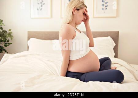 Schwangere Frau auf dem Bett zu Hause mit Kopfschmerzen Stockfoto