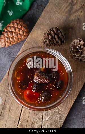 Junge Tannenzapfen verklemmen sich in einer Glasschale auf einem Holzbrett. Leckere Marmelade mit den kleinen Pinienzapfen. Stockfoto