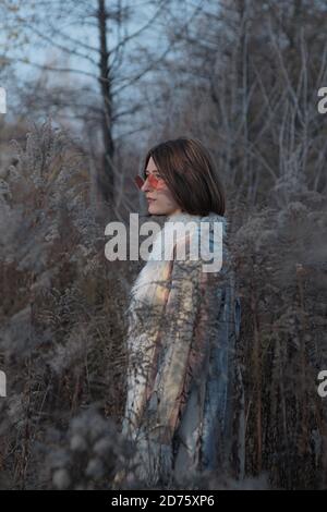 Porträt einer Frau im Hippie-Mantel und roter Sonnenbrille Unter Unkraut Stockfoto