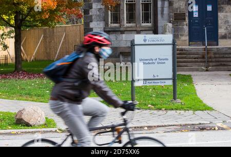 Toronto, Kanada. Oktober 2020. Eine Frau, die eine Gesichtsmaske trägt, fährt am 20. Oktober 2020 mit dem Fahrrad an der Students' Union der University of Toronto in Toronto, Kanada, vorbei. Unter neuen Ausnahmen von Kanadas Coronavirus-Reisebeschränkungen können internationale Studenten, die anerkannte Hochschulen und Universitäten besuchen, ab Oktober 20 nach Kanada reisen. Um nach Kanada zugelassen zu werden, müssen internationale Studierende, die für eine Studiengenehmigung zugelassen sind, an einer Designated Learning Institution mit einem COVID-19-Bereitschaftsplan teilnehmen, der von ihrer Provinz- oder Gebietsregierung genehmigt wurde. Quelle: Zou Zheng/Xinhua/Alamy Live News Stockfoto